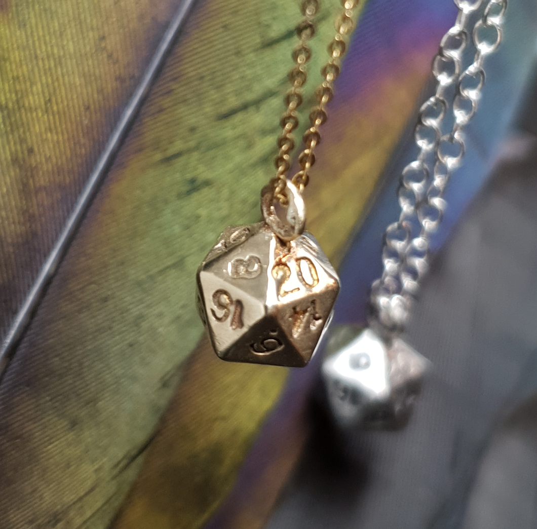 Solid 9ct gold D20 dice on a gold chain with a sterling silver one out of focus in the background. 